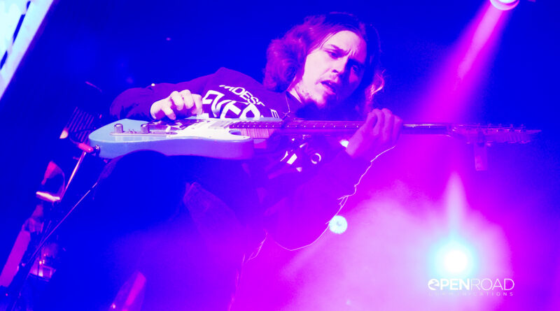 Daniel Donato leaning back while playing guitar bathed in purple hues