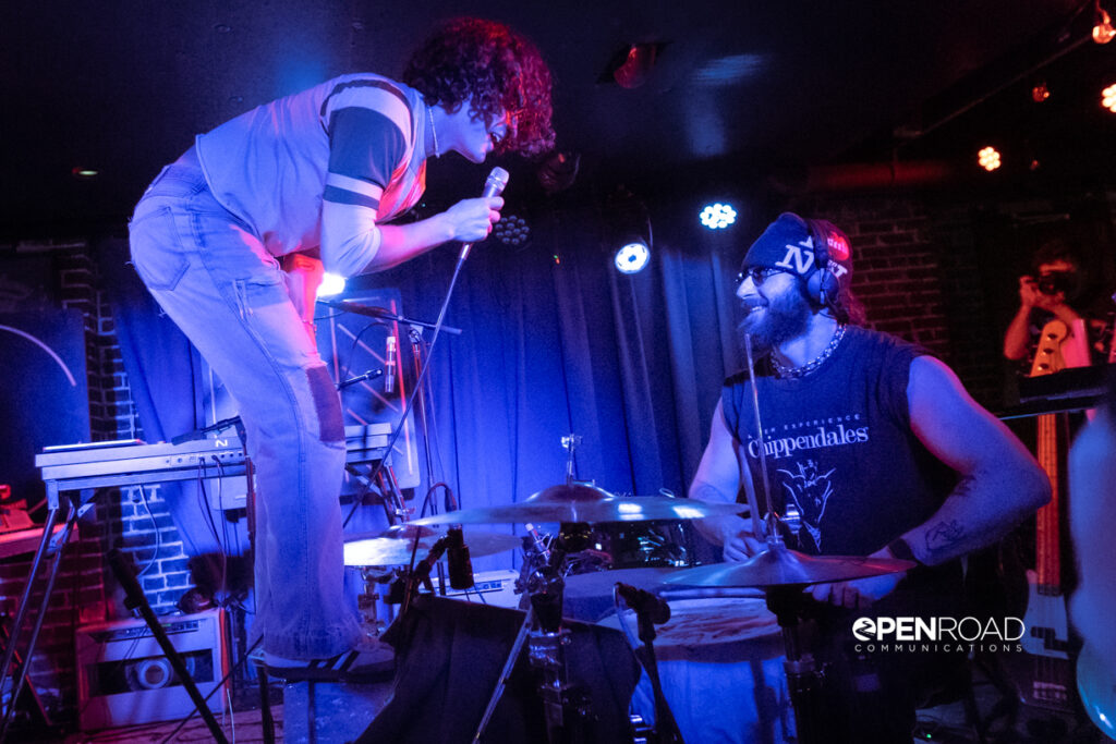 Zach Britt stands on the bass drum singing to the drummer