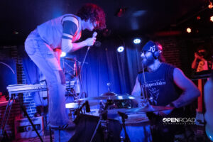 Zach Britt stands on the bass drum singing to the drummer