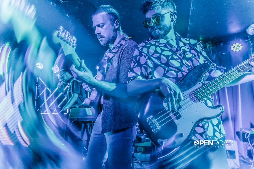 Bassist and guitarist stand back to back playing their instruments