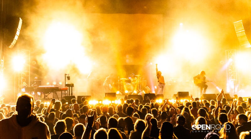 Wide shot of the band, Celebration Day on stage. Lots of yellows/warmth to the image.