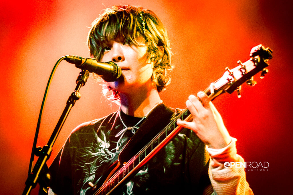 Mei Semones, bathed in orange hues singing at the mic while playing guitar at her St. Louis concert