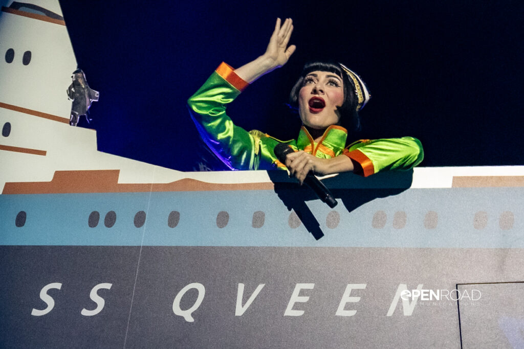 Qveen Herby, in a bright green raincoat, sings with aboard the SS Qveen