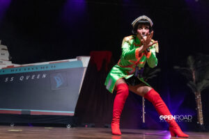Qveen Herby crouching over, extends a hand while singing into a hand held microphone.