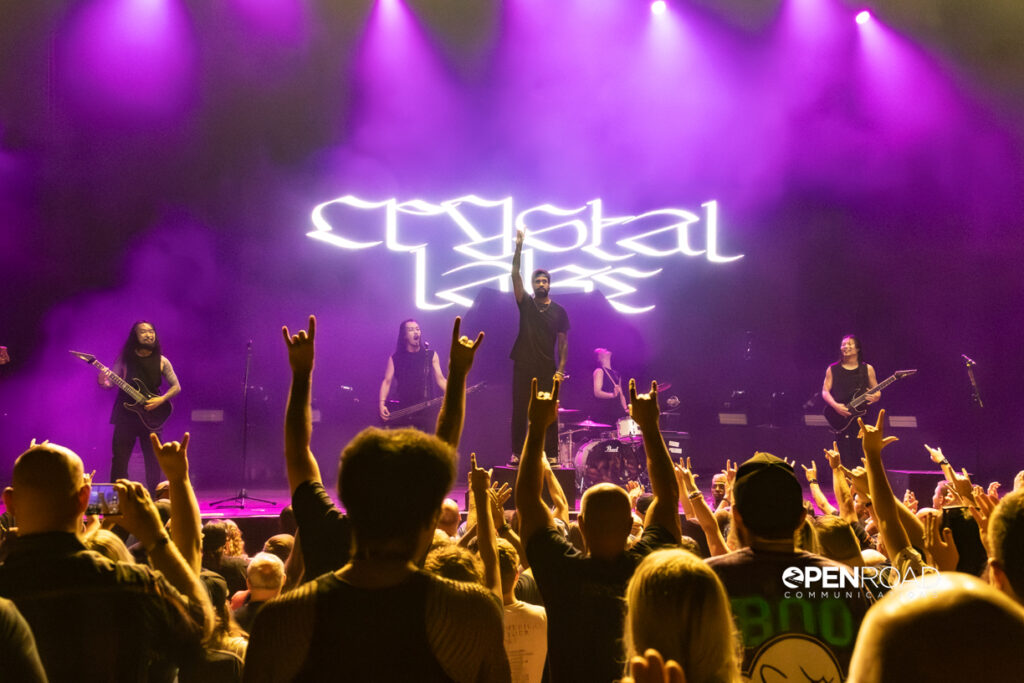 wide shot showing members of Crystal Lake on stage. Excited fans have their hands in the air.