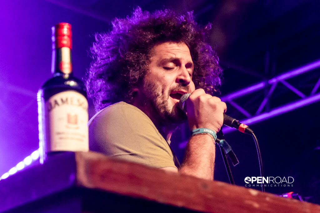 Andy Frasco sings into the mic. The ever-present bottle of whiskey on the piano