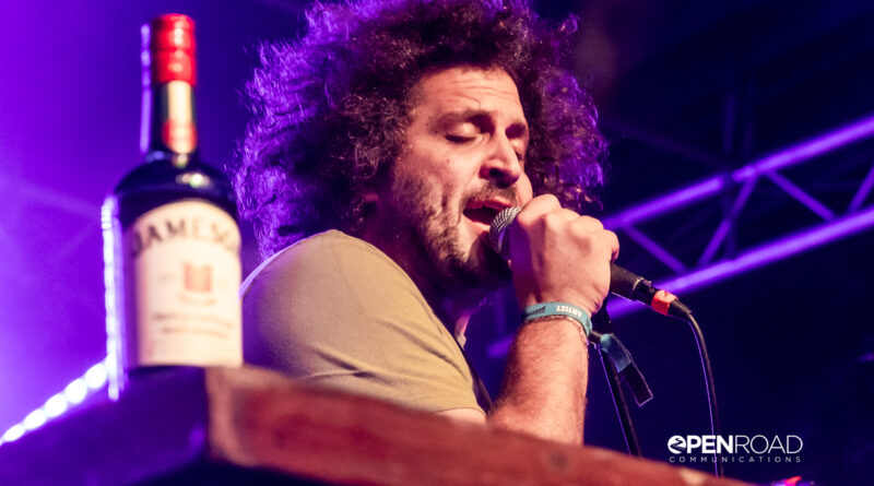 Andy Frasco sings into the mic. The ever-present bottle of whiskey on the piano