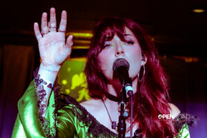 Kitty Coen holds her hand up while singing into the mic